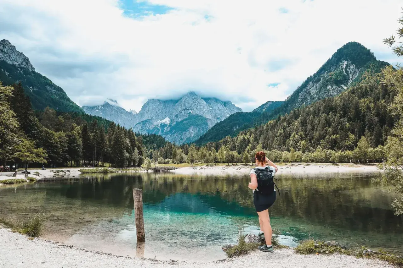 Frau mit Rucksack genießt den Blick auf einen türkisfarbenen See und die Berge. Perfekter Ort zum Wandern in Slowenien.