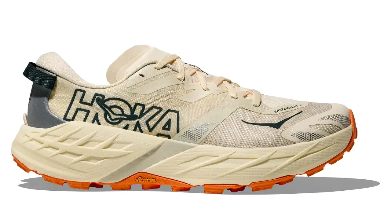 Beiger Hoka Speedgoat 7 Trailrunningschuh mit orangefarbener Vibram-Sohle und dunklem Hoka-Logo.