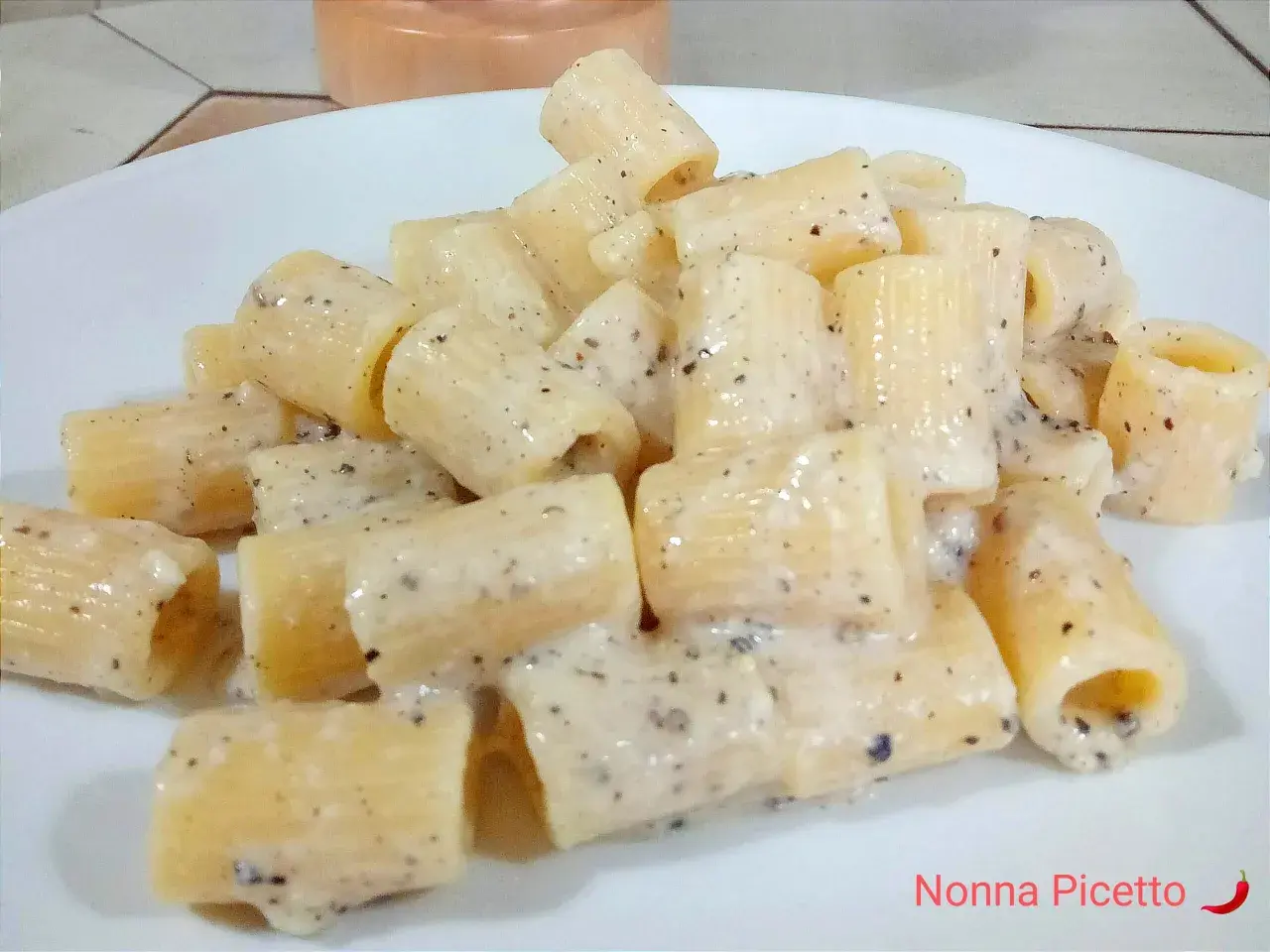 Un piatto di pasta cacio e pepe, con rigatoni cremosi e pepe nero macinato.