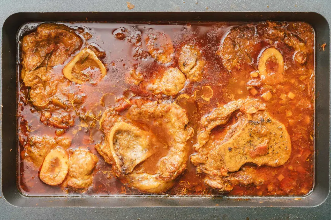 Herzhaftes Ossobuco-Rezept original italienisch: Kalbshaxenscheiben schmoren in aromatischer Sauce mit Gemüse und Kräutern in einer Bratpfanne.