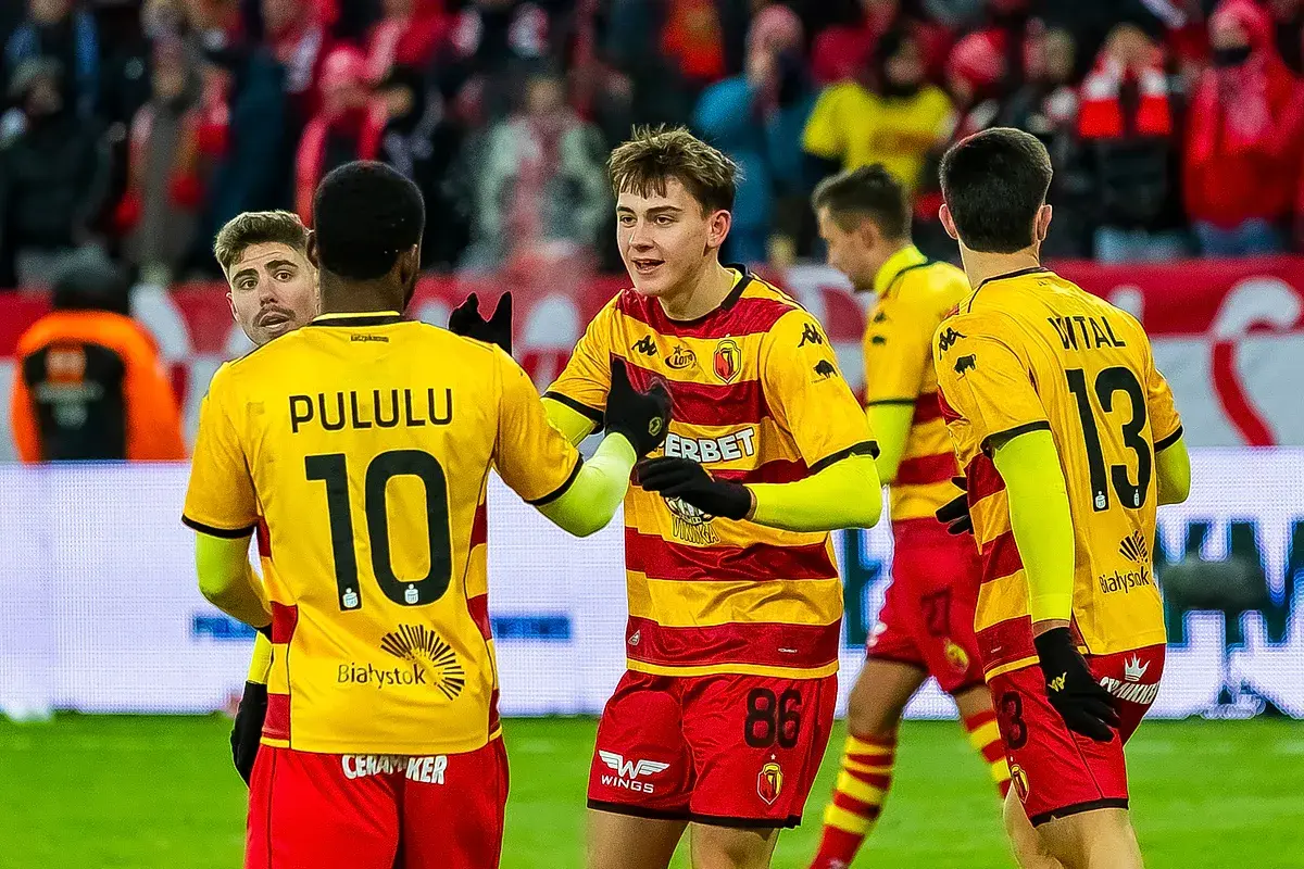 Piłkarze Jagiellonii Białystok świętują. Na boisku w meczu przeciwko Górnikowi Zabrze, zawodnicy w żółto-czerwonych strojach cieszą się z sukcesu.