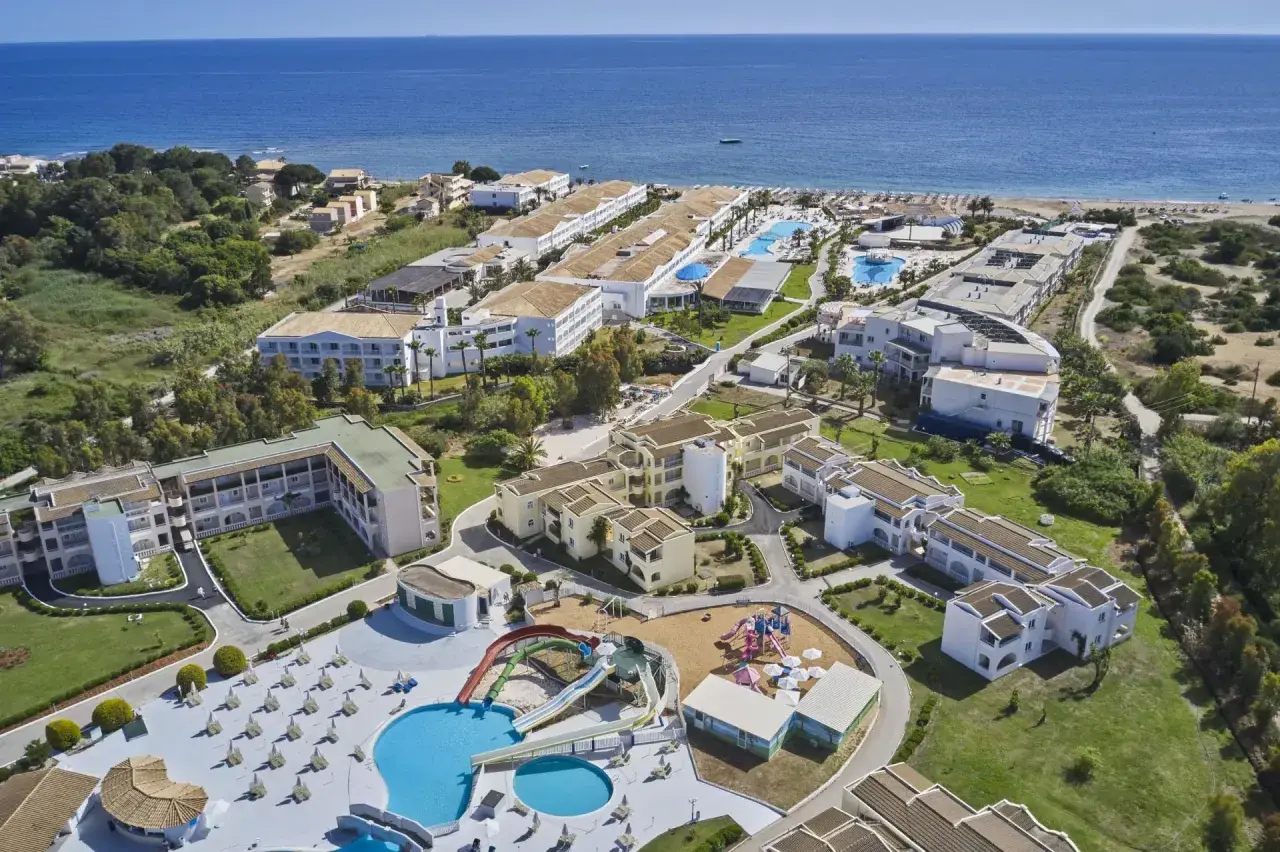 Widok z lotu ptaka na kompleks hotelowy z basenami, zjeżdżalniami i placem zabaw, blisko plaży. Wiele budynków, zieleni i morza. Idealne miejsce na wakacje, zgodnie z labranda sandy beach resort opinie.