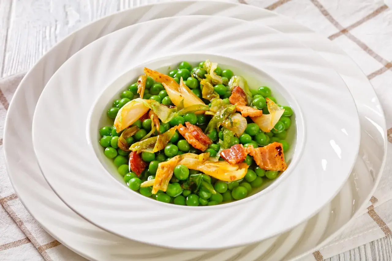 Un plat de petit pois à la française, garni de lardons croustillants et de légumes tendres, servi dans une assiette blanche élégante.
