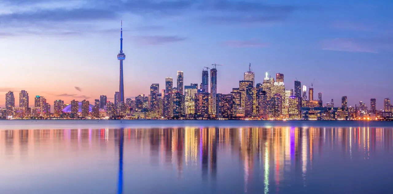 Toronto Skyline bei Dämmerung, ein Muss für jeden Besucher. Der CN Tower ragt empor, beleuchtete Wolkenkratzer spiegeln sich im Wasser.