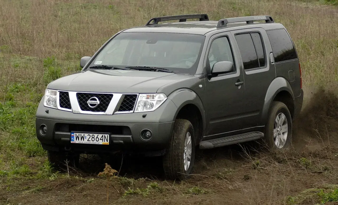 Szary Nissan Pathfinder r51 pokonuje błotniste wzniesienie, wzbijając tumany kurzu.