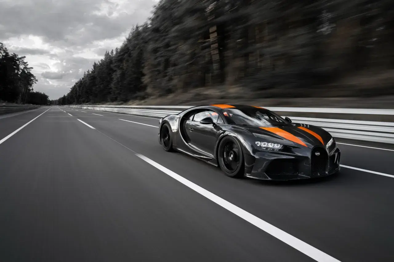 Czarny Bugatti Chiron Super Sport z pomarańczowymi pasami pędzi po pustej autostradzie.