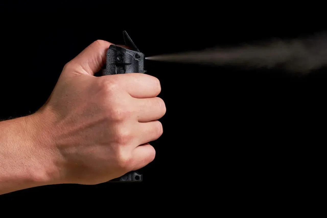 Main d'une personne actionnant une bombe lacrymogène, le jet de gaz se dispersant dans l'air. La loi encadre l'usage de ce type de défense.