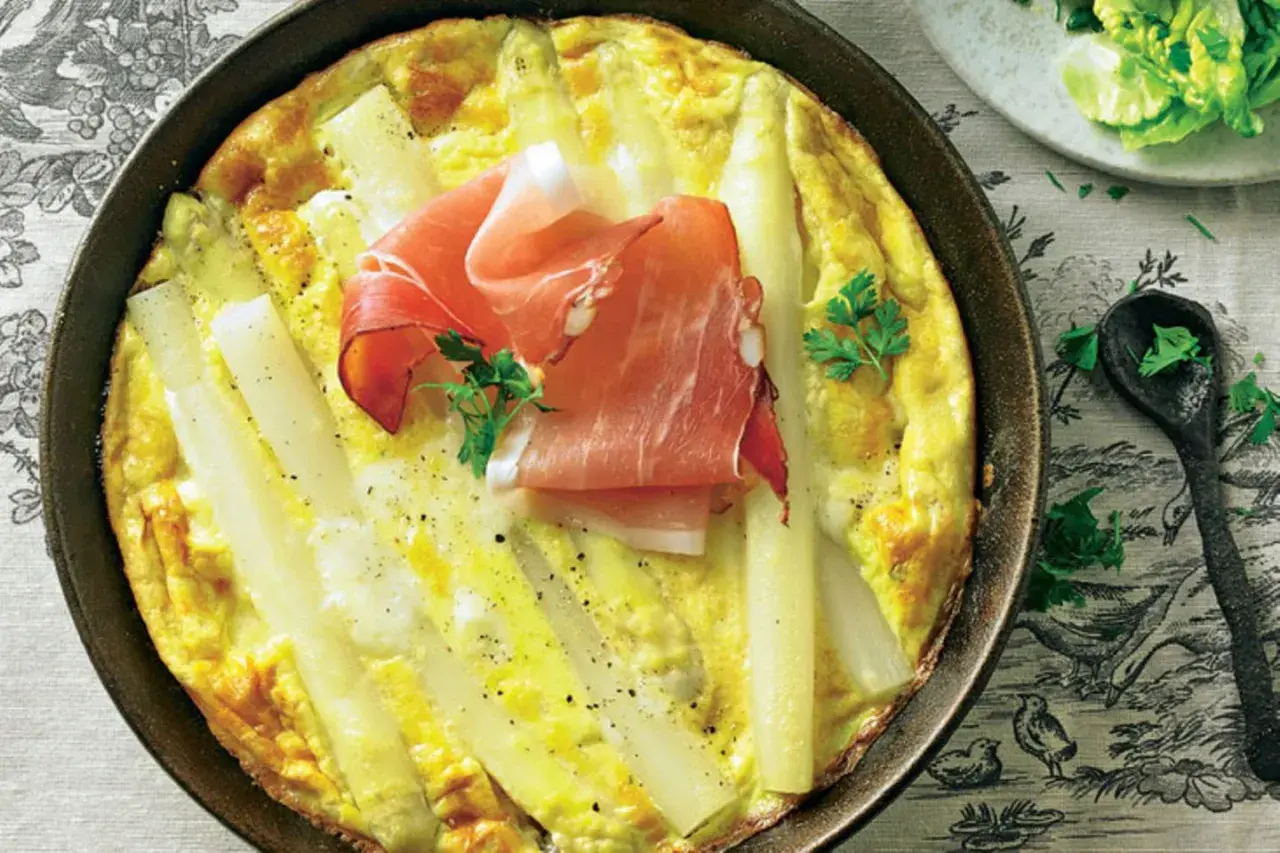 Spargel-Frittata mit Schinken in einer Pfanne, garniert mit Petersilie.