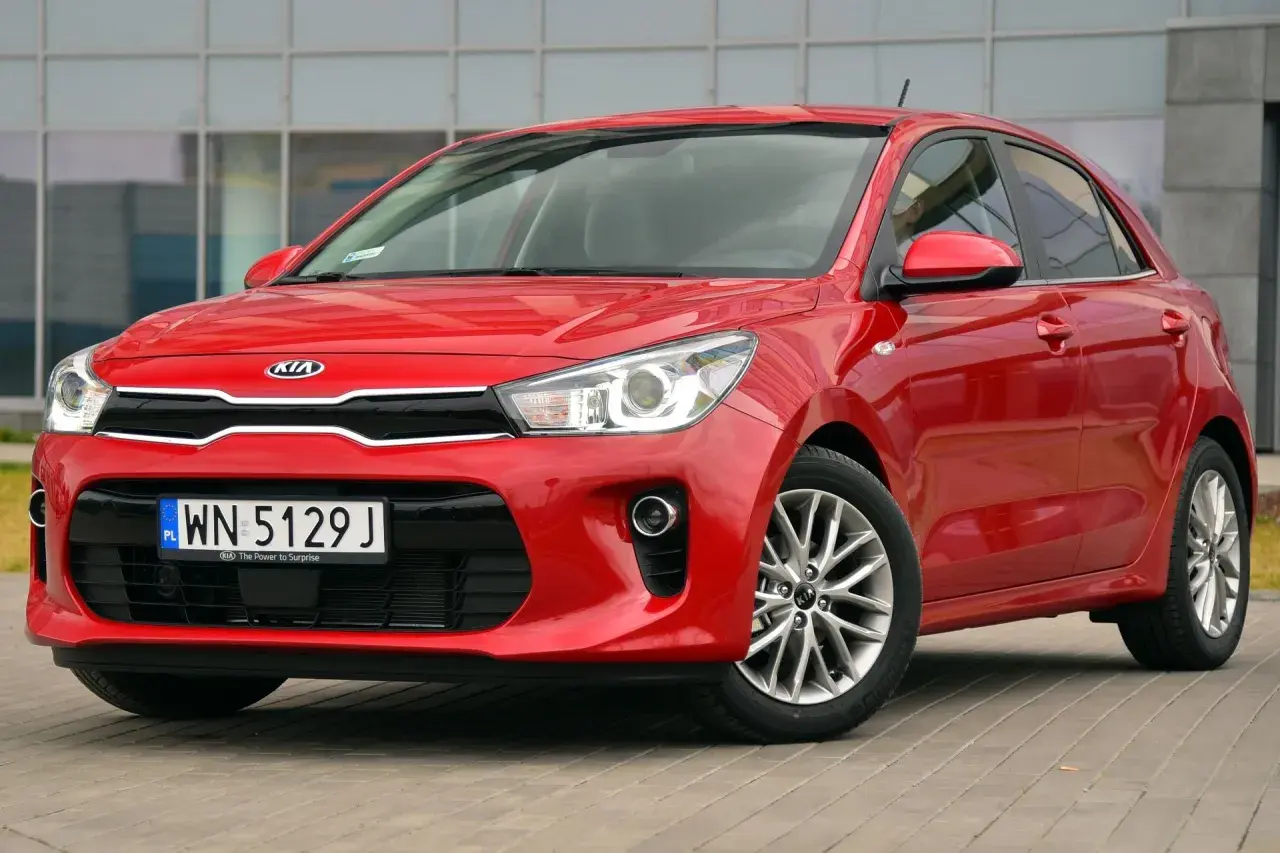 Czerwone Kia Rio przed budynkiem. Wymiana żarówki do jazdy dziennej w tym modelu jest prosta.