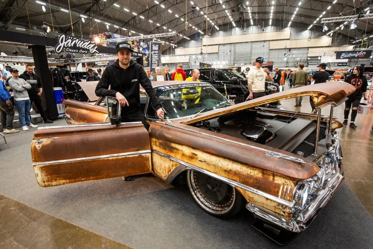 Man bredvid en rostig Oldsmobile 1955 med öppen dörr och motorhuv. Bilen har kromdetaljer och djupa fälgar.