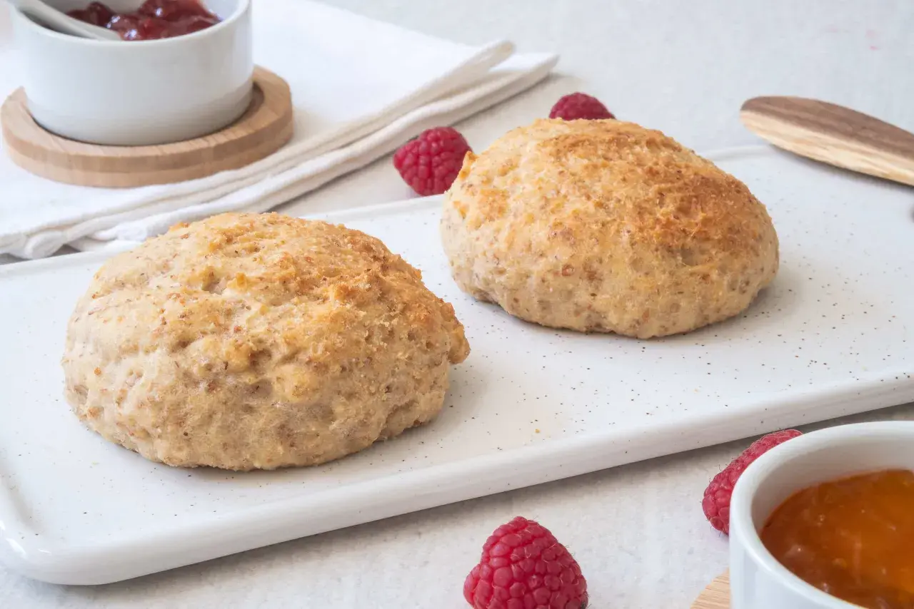 Två gyllene scones på en vit bricka, med hallon och sylt. Perfekt för fika med de godaste scones.