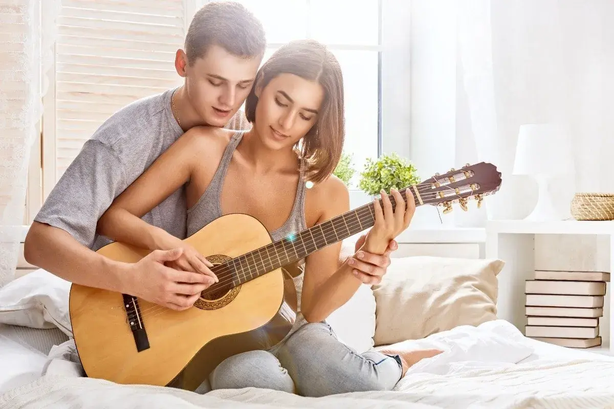 Para tworzy najpiękniejsze melodie o miłości, grając razem na gitarze w przytulnym pokoju.