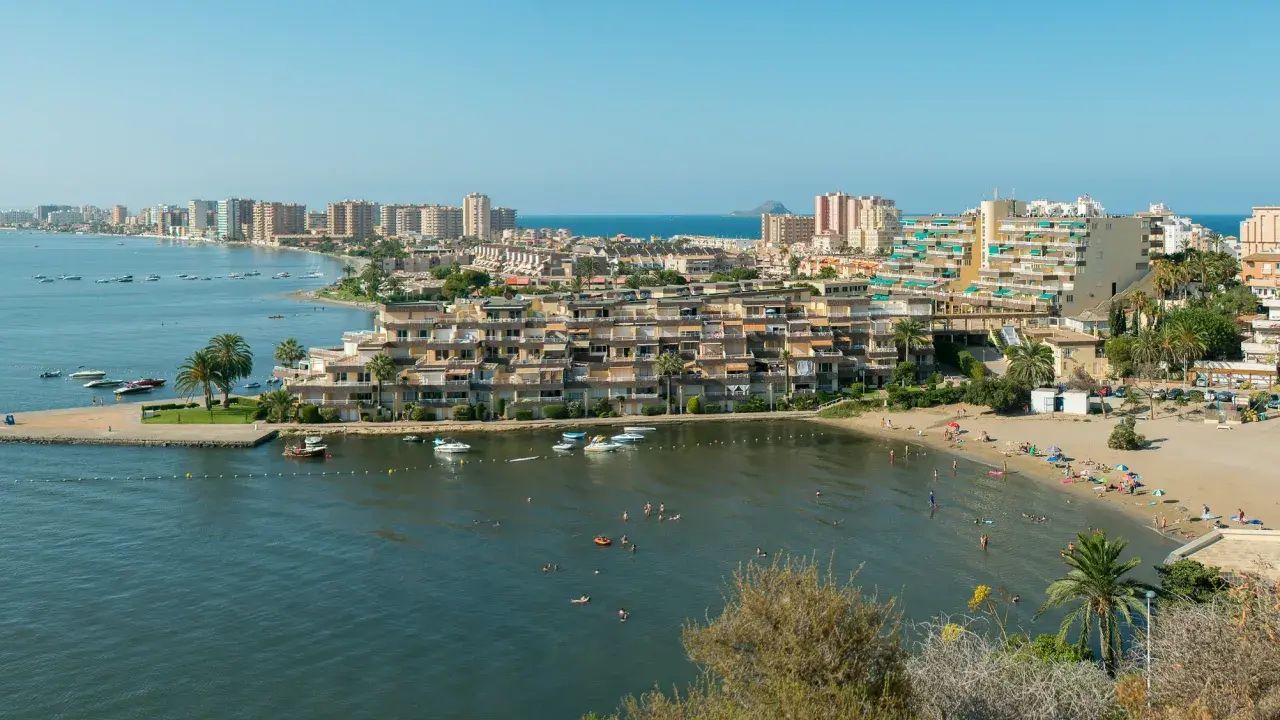 Widok na La Mangę z plażą, budynkami mieszkalnymi i łodziami na wodzie.