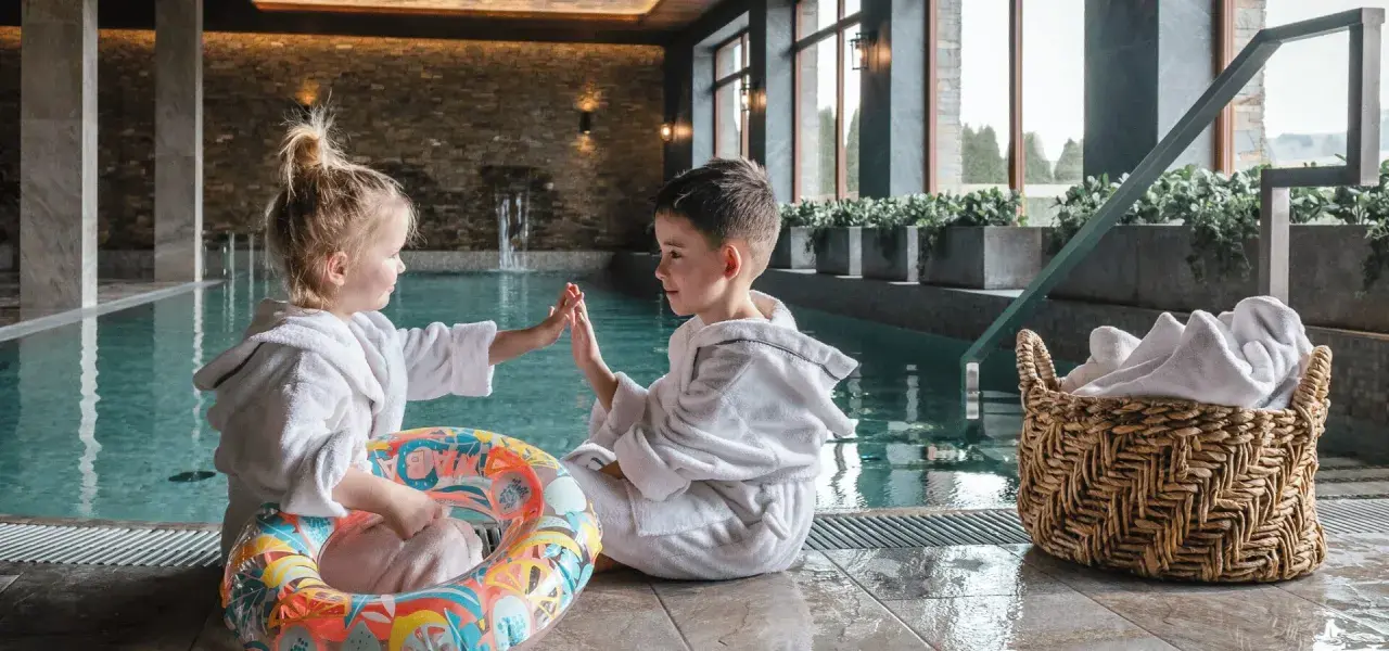 Dzieci w szlafrokach przy basenie, gotowe na wakacje w górach z dziećmi. Zabawa i relaks w górskim spa.