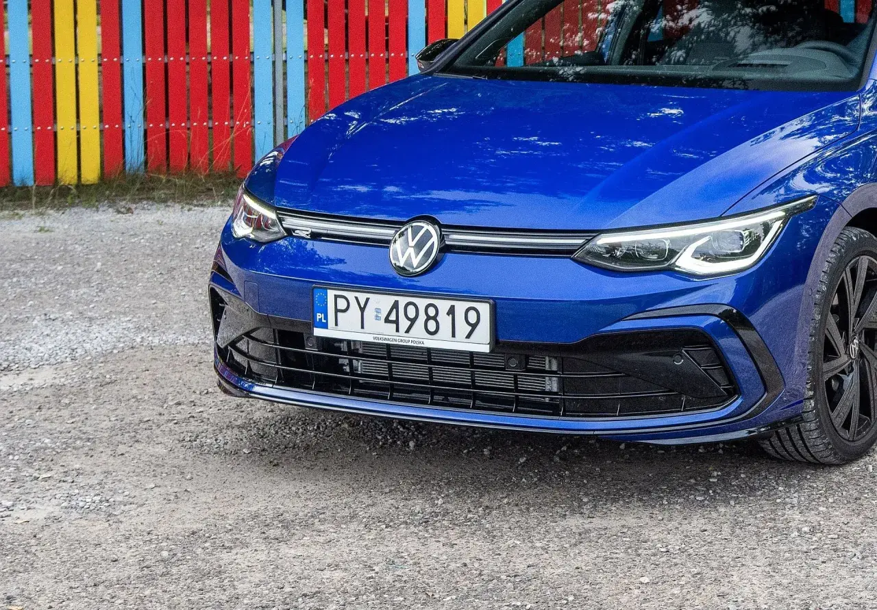 Niebieski Volkswagen z rejestracją PY 49819 stoi przed kolorowym płotem.