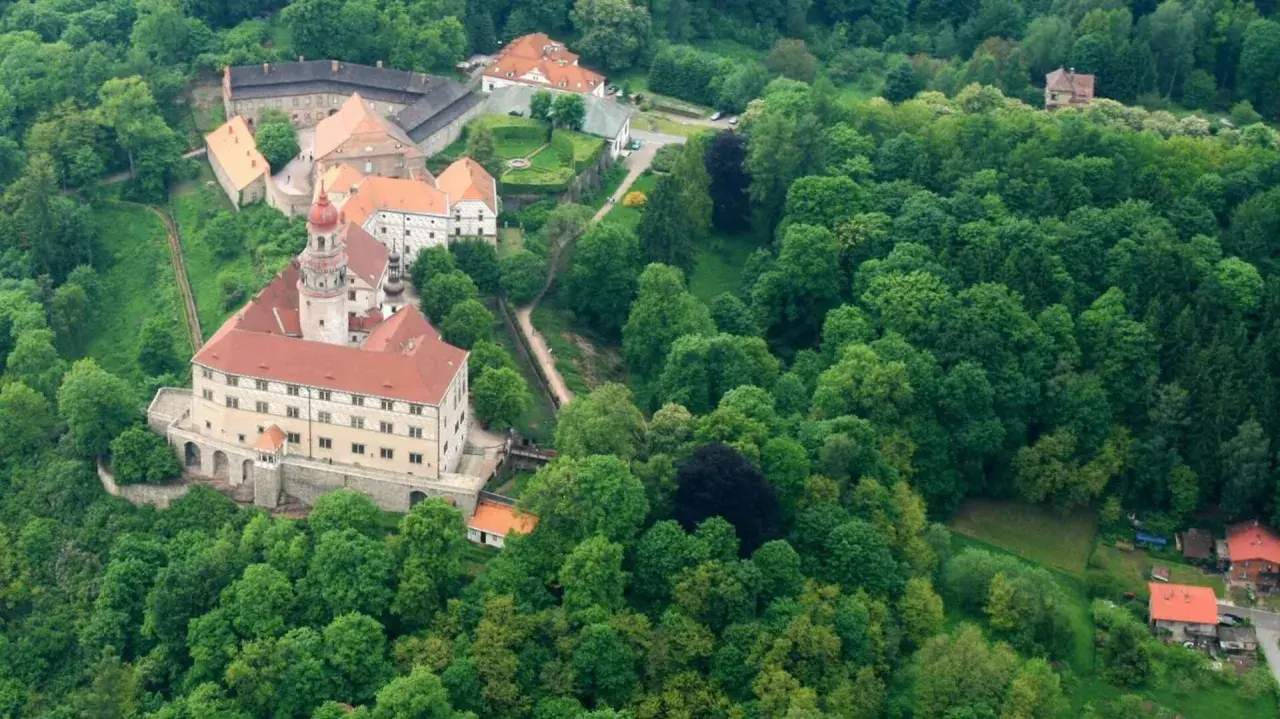 Zamek Nachod w Czechach, otoczony bujną zielenią, z charakterystyczną wieżą i czerwonymi dachami.