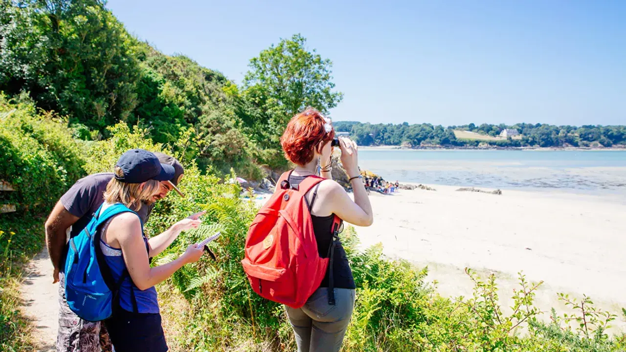 Couple en randonnée à Saint-Jacut-de-la-Mer, consultant une carte. Une femme observe la baie avec des jumelles.