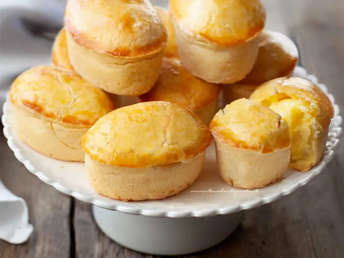 Un mucchio di pasticciotti pugliesi dorati e invitanti su un alzatina bianca.