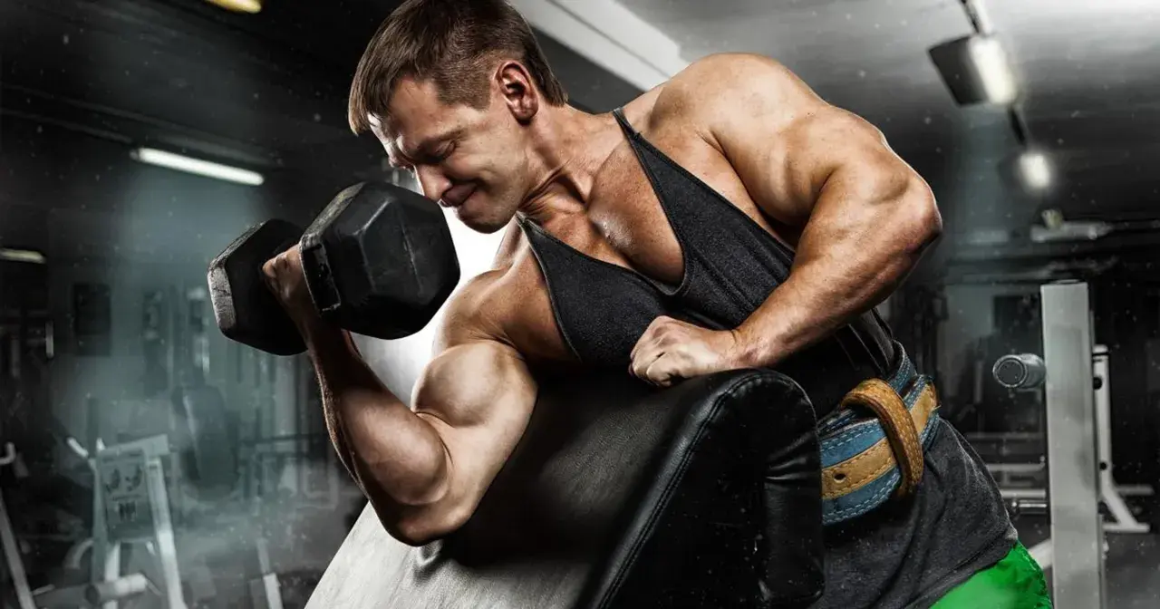 Mężczyzna z determinacją ćwiczy biceps, napinając mięsień trójgłowy ramienia z ciężarem.