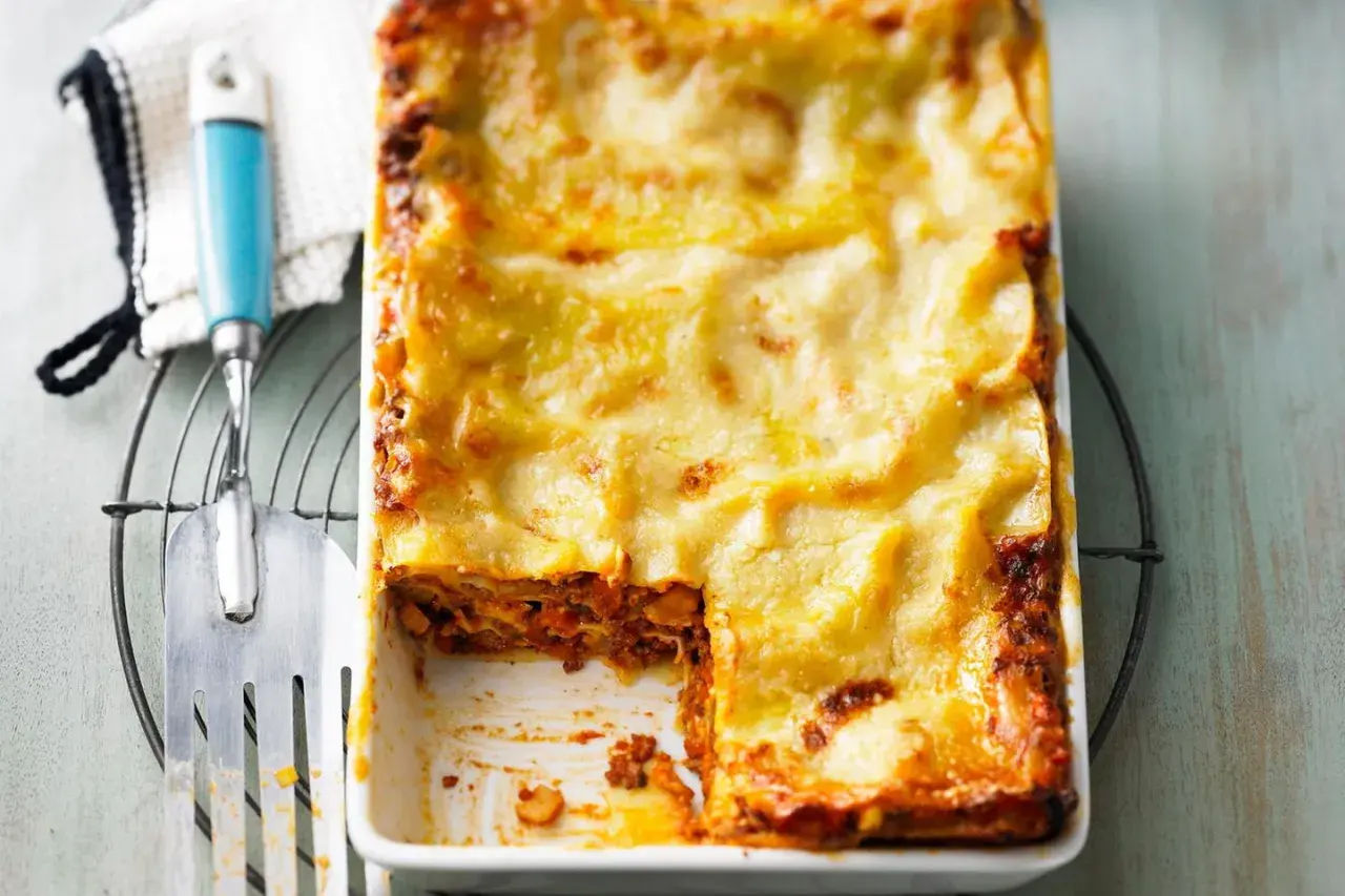Eine frisch gebackene Lasagne in einer Auflaufform, mit einem Stück herausgeschnitten.