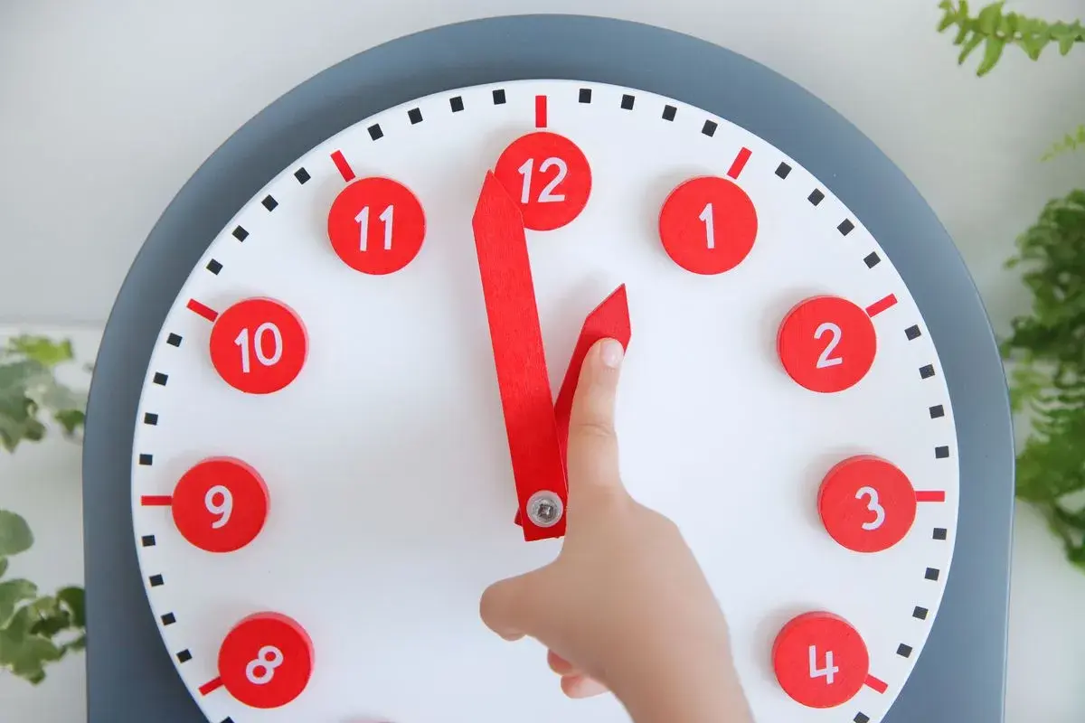 Un niño aprende las horas con un reloj didáctico. Las manecillas rojas apuntan a las 12 y las 11.