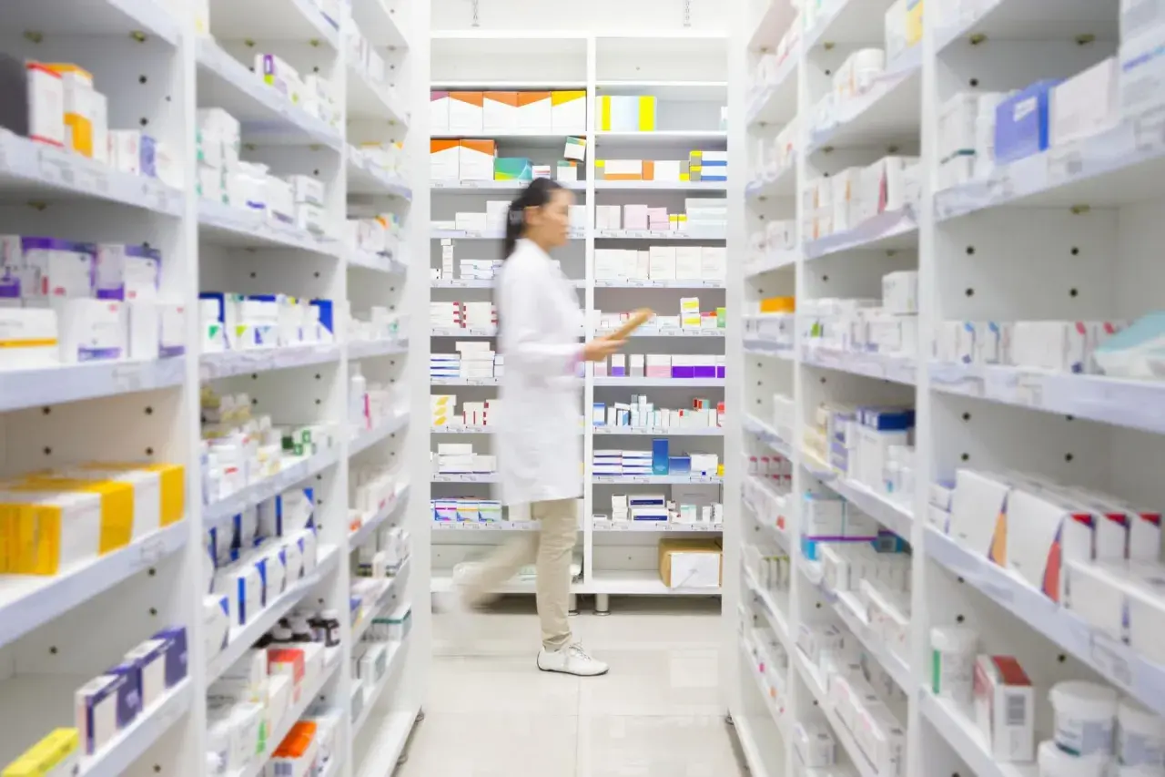 Farmaceutka w białym fartuchu przeszukuje półki apteki, szukając leku milurit 300.