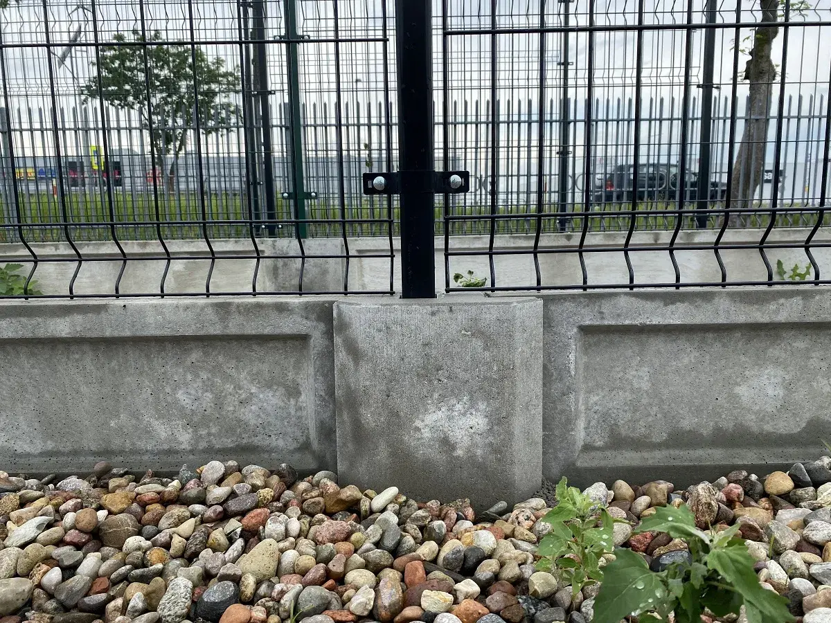 Solidny montaż podmurówki na ceowniku, zabezpieczający teren. Kamienie i beton tworzą trwałą podstawę dla ogrodzenia.