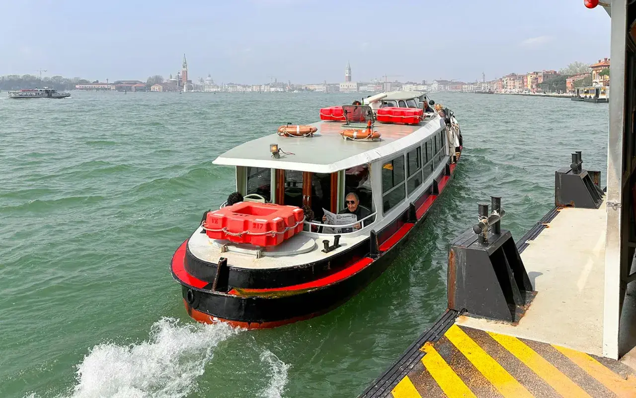En man läser tidningen på en av båtarna i Venedig. I bakgrunden syns stadens silhuett.