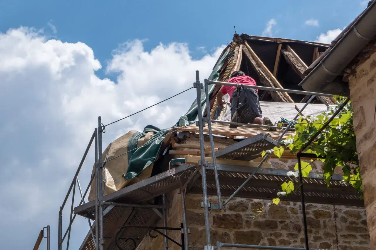 Un ouvrier travaille sur un toit en rénovation, une étape essentielle pour garantir ma prime logement décent. Le ciel bleu et les nuages blancs surplombent le chantier.
