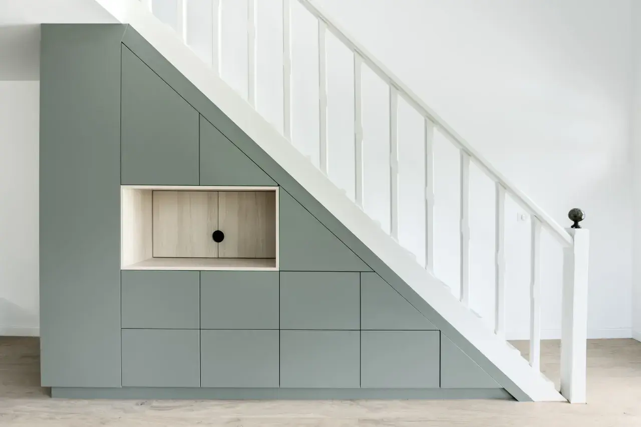 Aménagement sur mesure : un rangement sous escalier gris pâle avec des portes et une niche en bois clair.