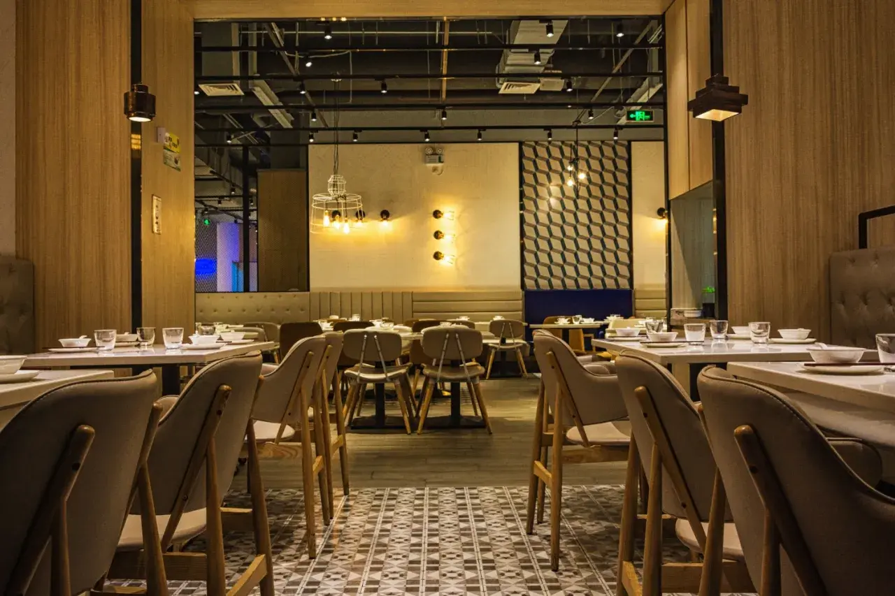Przytulne wnętrze restauracji z drewnianymi panelami i stylowym oświetleniem. Stoliki nakryte, gotowe na gości.