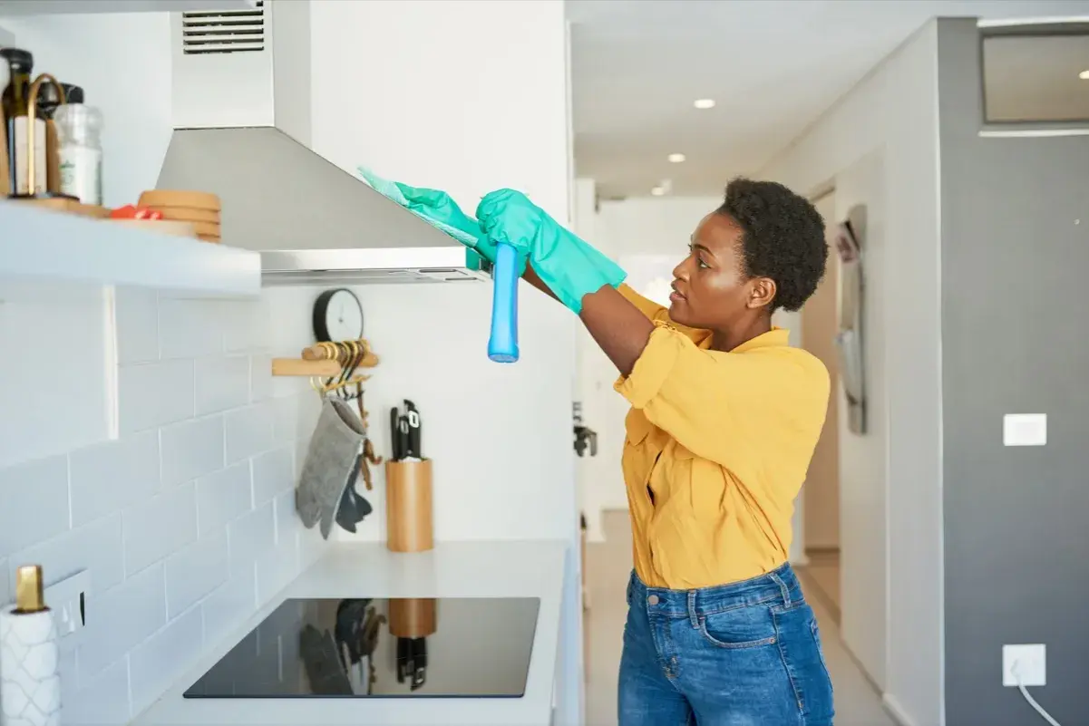 Donna con guanti pulisce la cappa della cucina con uno spray.
