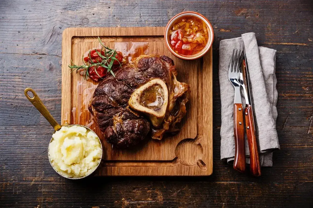 Wołowe ossobuco z puree ziemniaczanym, sosem i gałązką rozmarynu na desce.