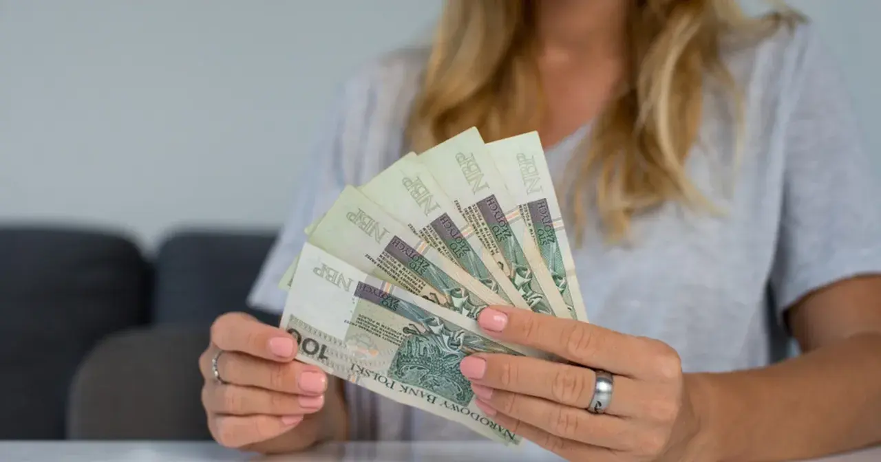 Kobieta trzyma w rękach banknoty 100 zł. To może być symbol dodatkowych 200 zł do emerytury za dzieci.