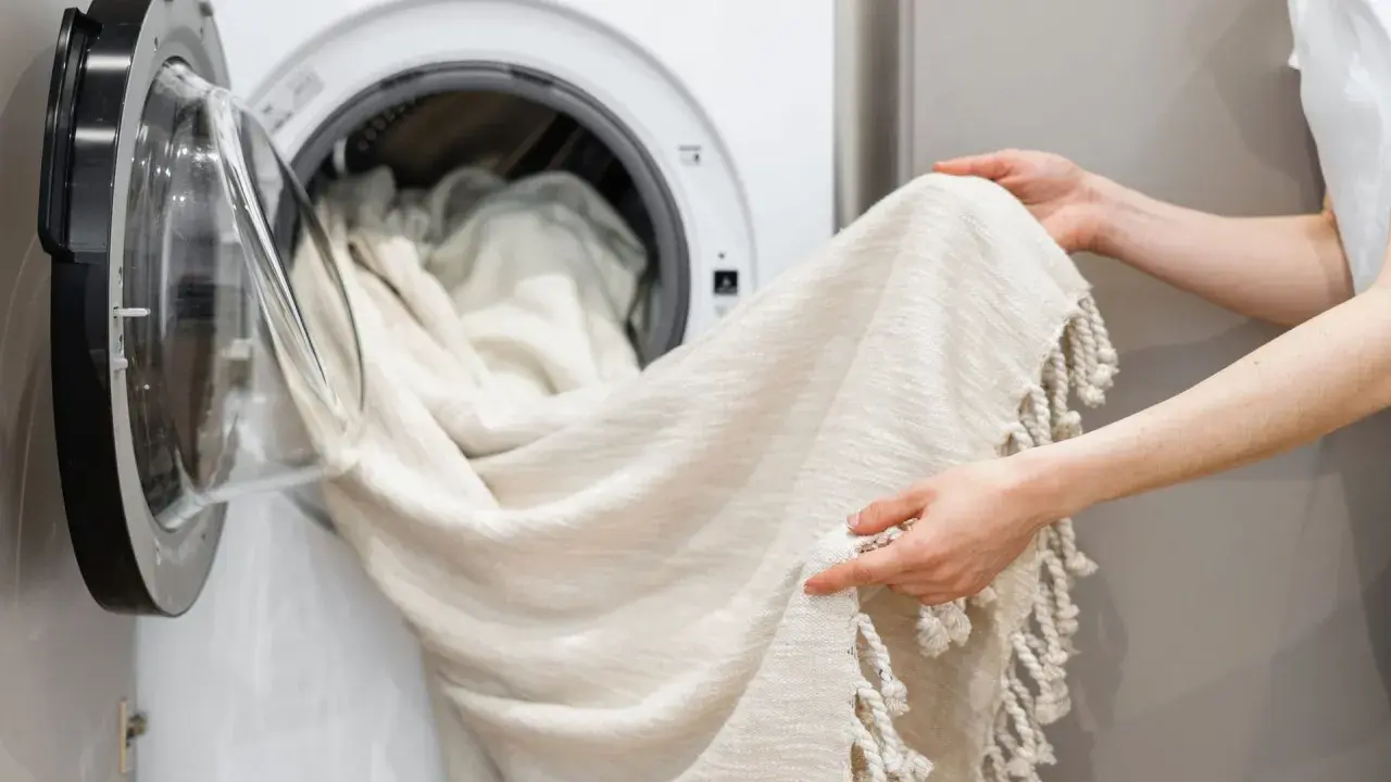 Helle Gardinen werden in die Waschmaschine geladen. Ein Hausmittel wie Backpulver kann helfen, sie wieder strahlend weiß zu machen.