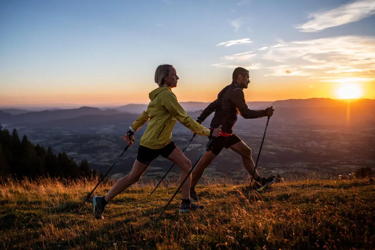 Para uprawiająca nordic walking na tle zachodzącego słońca nad górami.
