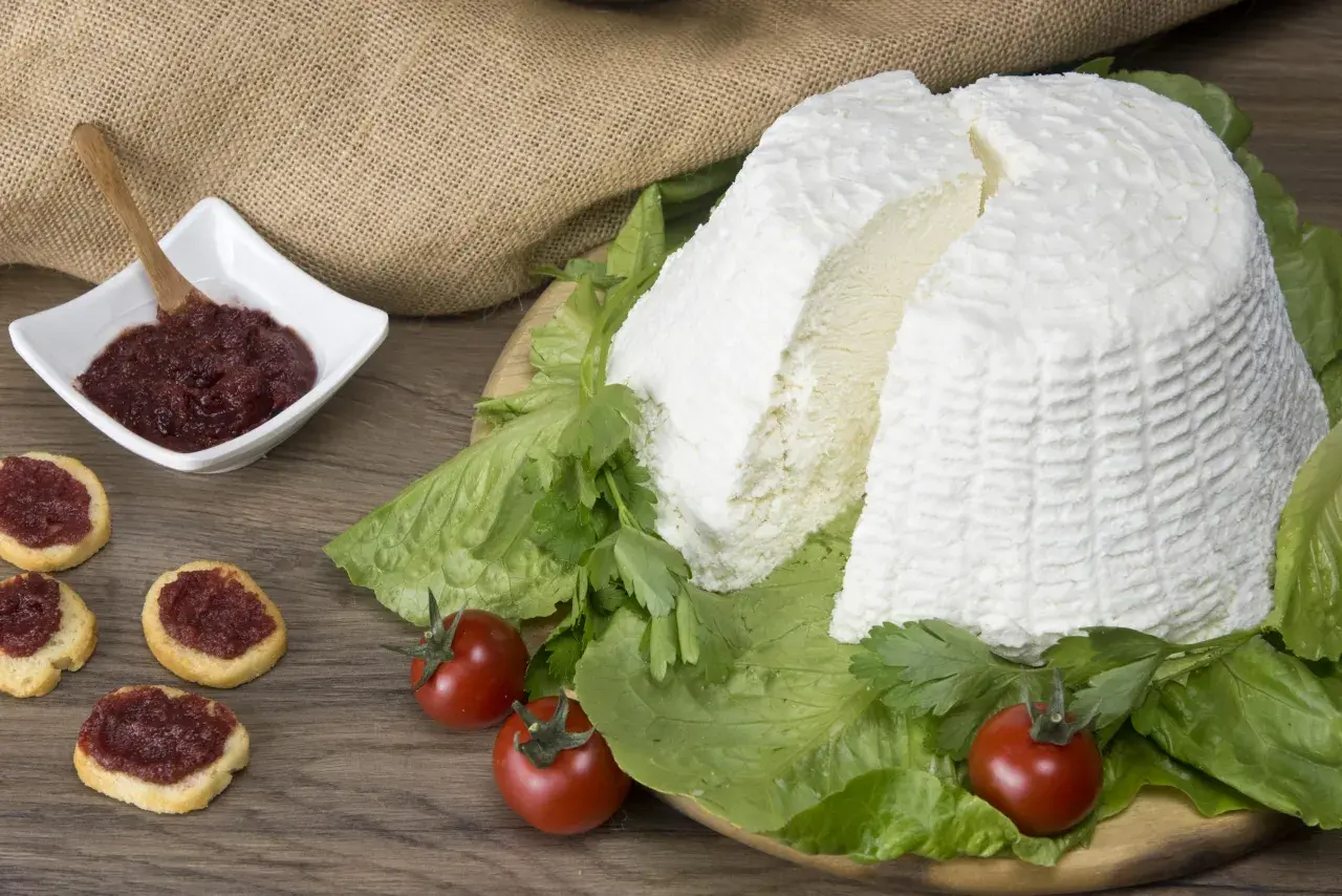 Un grande blocco di ricotta fresca, circondato da lattuga e pomodorini, con bruschette e marmellata in una ciotola. Diversi tipi di ricotta sono presentati in modo invitante.