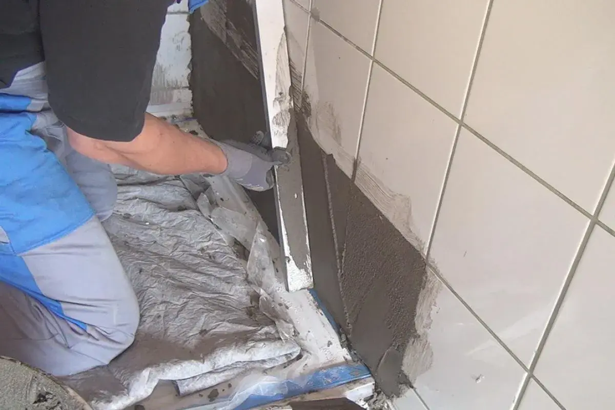 Hand mit Handschuh trägt Mörtel auf alte Fliesen auf, um eine Abdichtung zu schaffen.