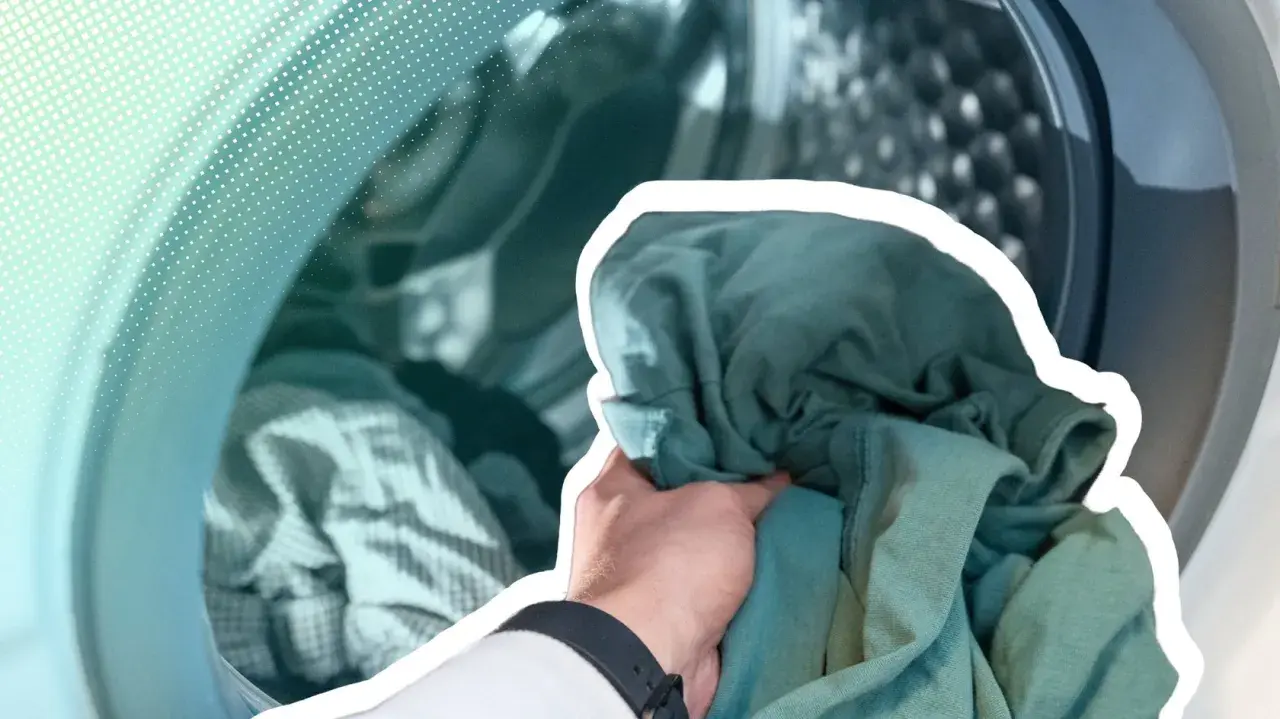 Hand lädt grüne Kleidung in eine Waschmaschine. Zeit, die neue Kleidung zu waschen und sie frisch zu machen.