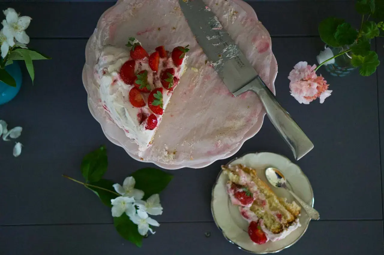 En bit av en läcker jordgubbstårta med grädde och färska jordgubbar. Ett perfekt jordgubbstårta recept för sommaren.