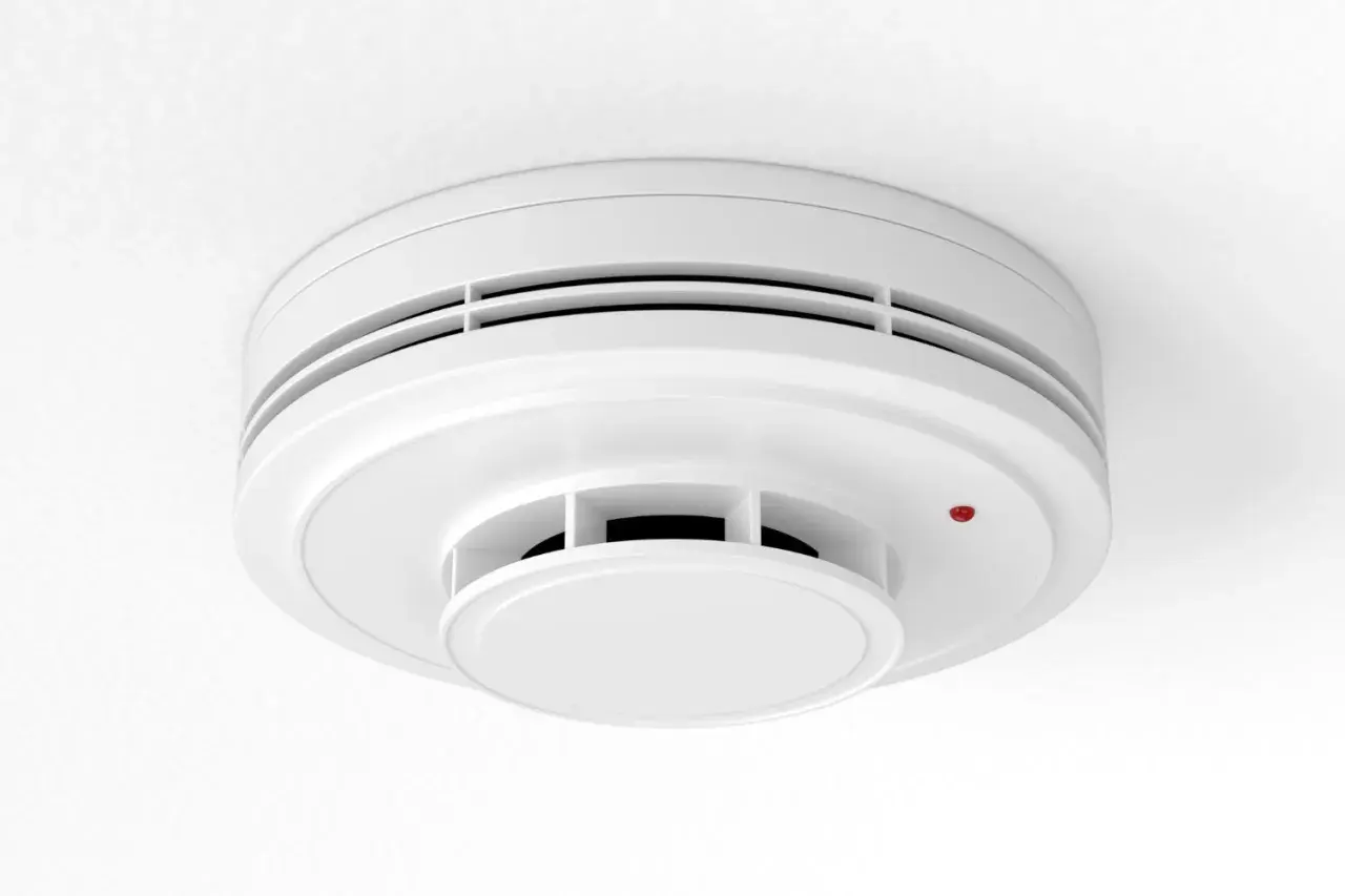 Détecteur de fumée blanc, rond, fixé au plafond. Un petit voyant rouge est allumé. Un détecteur fumée obligatoire pour votre sécurité.