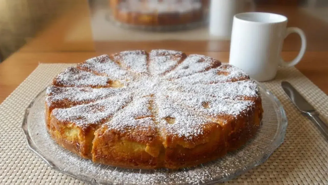 Gâteau fondant aux pommes et mascarpone, saupoudré de sucre glace, prêt à être dégusté avec une tasse de café.