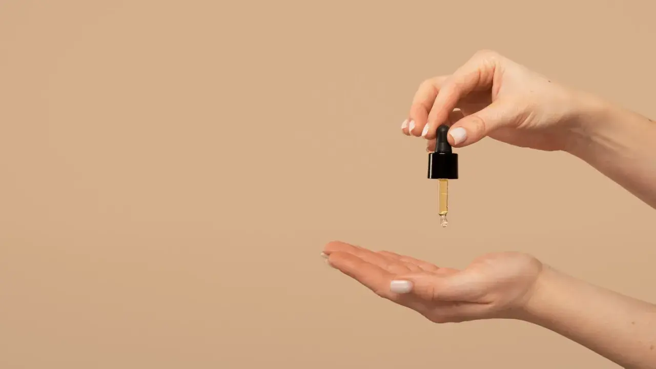 Una mano sostiene un gotero con aceite de jojoba para el pelo, listo para aplicarlo en la otra mano.