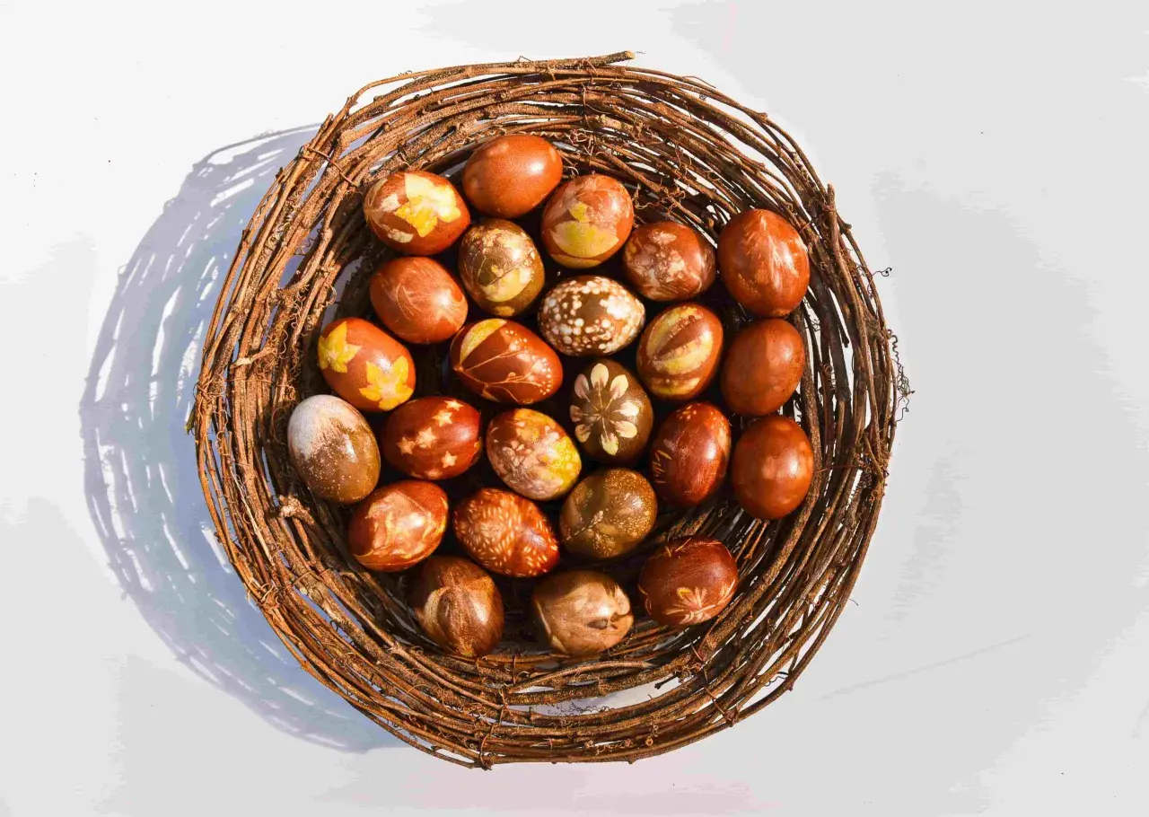 Pisanki w koszyku z gałęzi, barwione naturalnie w łupinach cebuli, z wzorami liści i kwiatów.