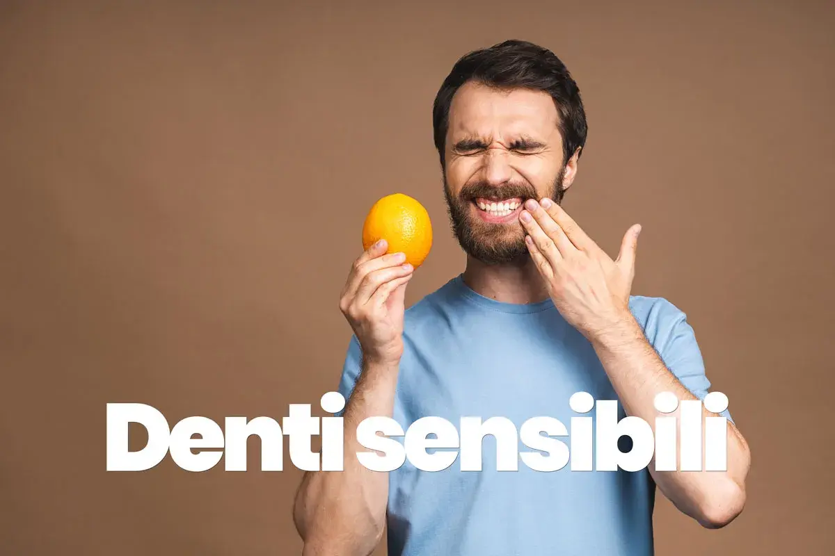 Uomo con espressione di dolore, tiene un'arancia e si tocca la guancia, soffre di sensibilità dentale.