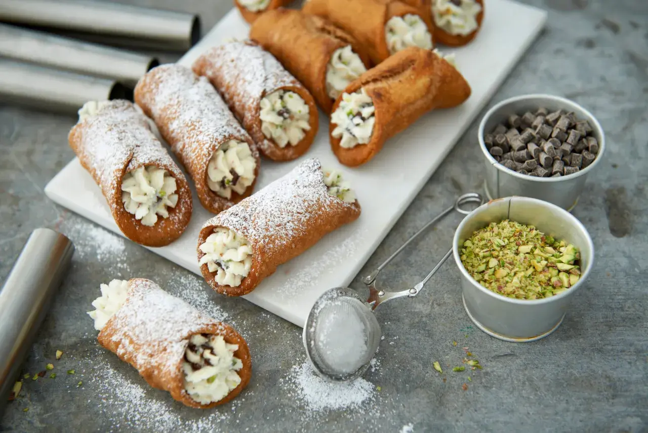 Färska cannoli med krämig fyllning, pudrade med florsocker. Ingredienser för ett perfekt cannoli recept syns bredvid.