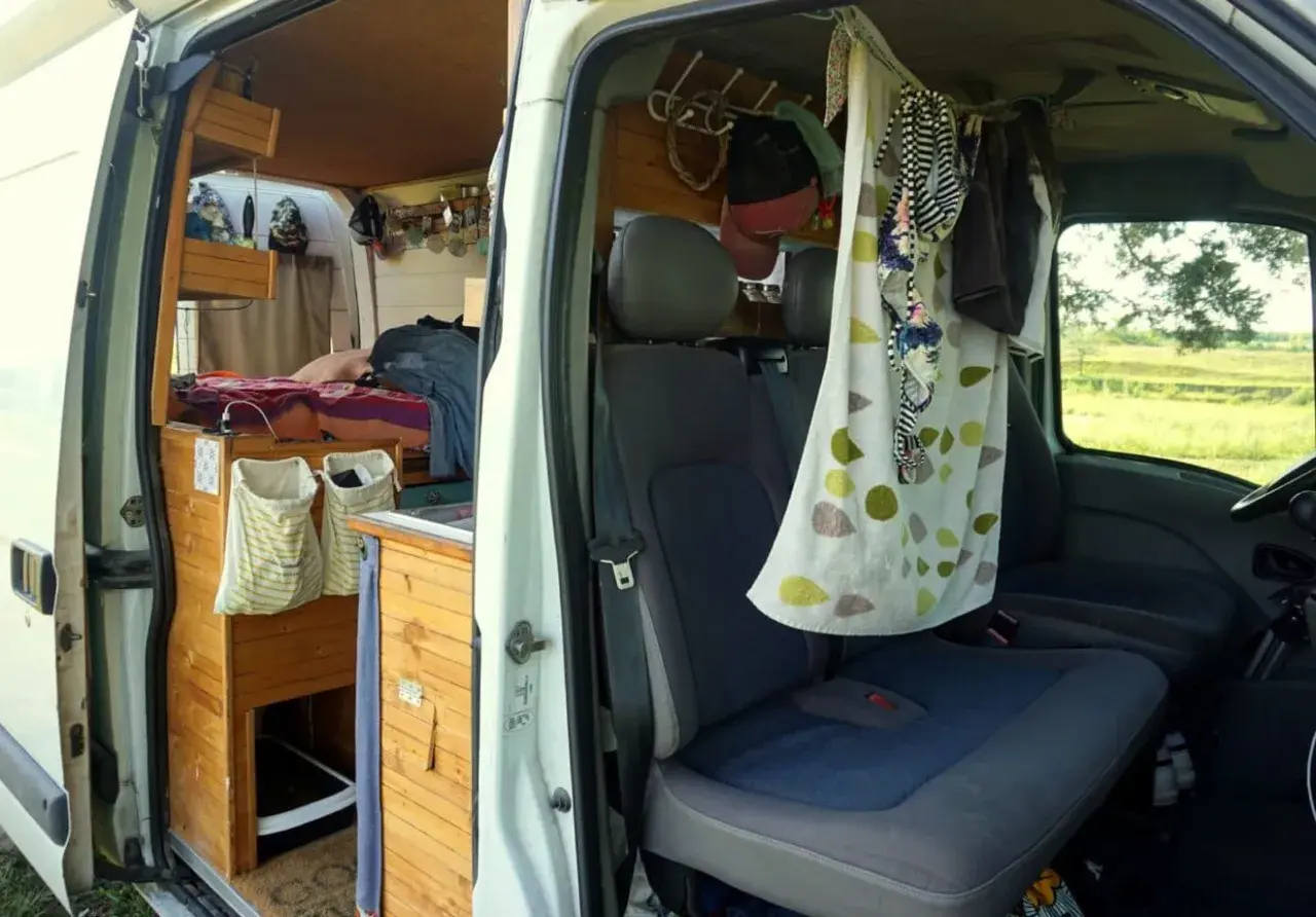 Aménagement d'un van pour 4 : lit, rangements en bois, sièges et rideau décoratif.