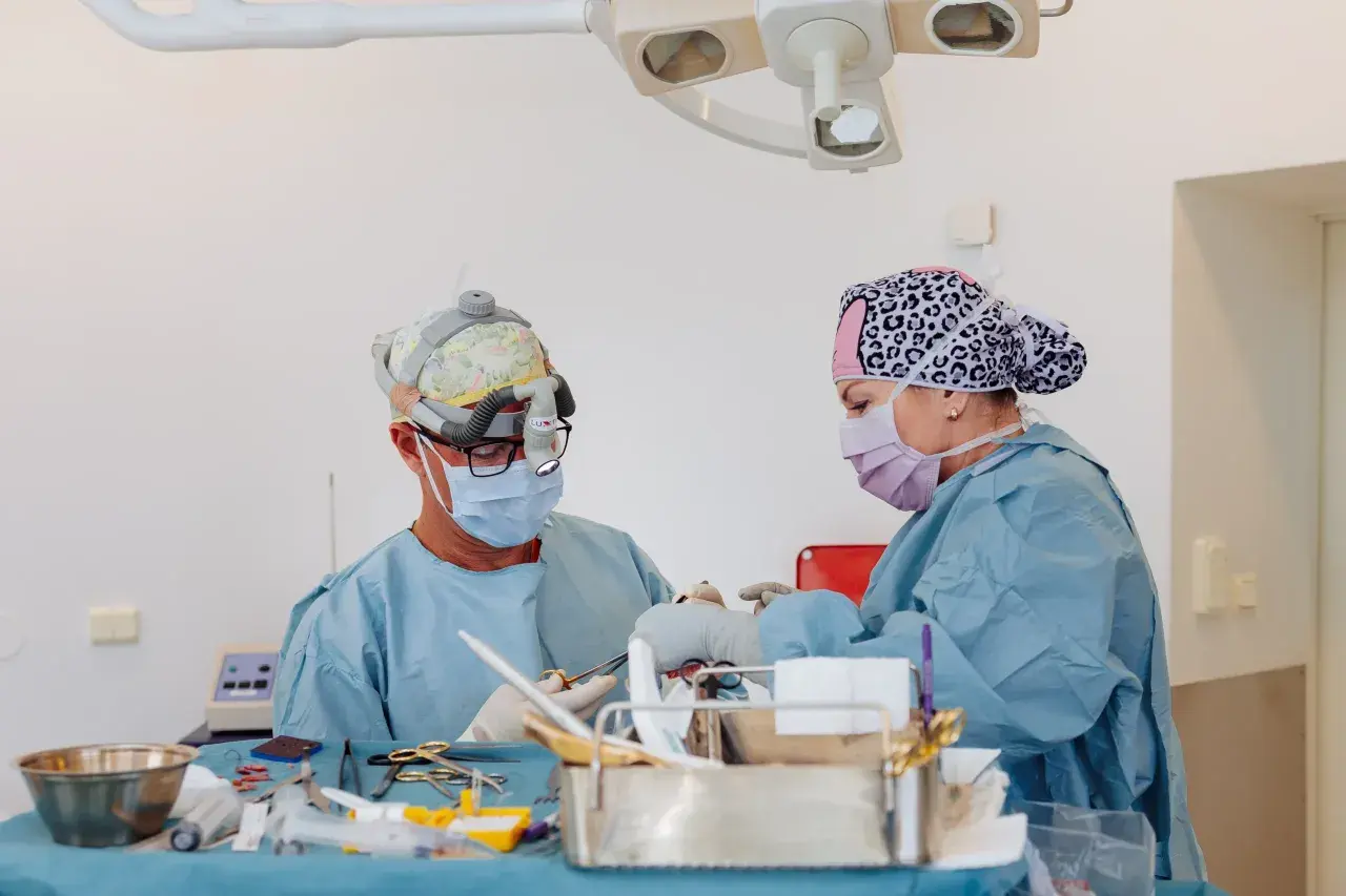 Två kirurger arbetar med instrument på ett bord. En av dem har en lampa på huvudet, vilket kan tyda på en komplicerad operation, kanske efter ett ansiktslyft.