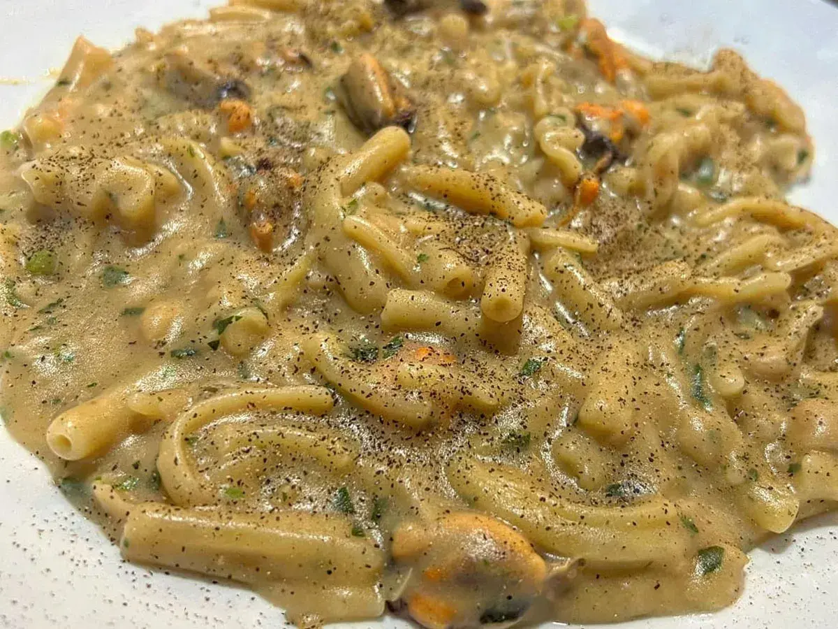 Un piatto cremoso di pasta fagioli e cozze, condito con prezzemolo fresco e pepe nero macinato.