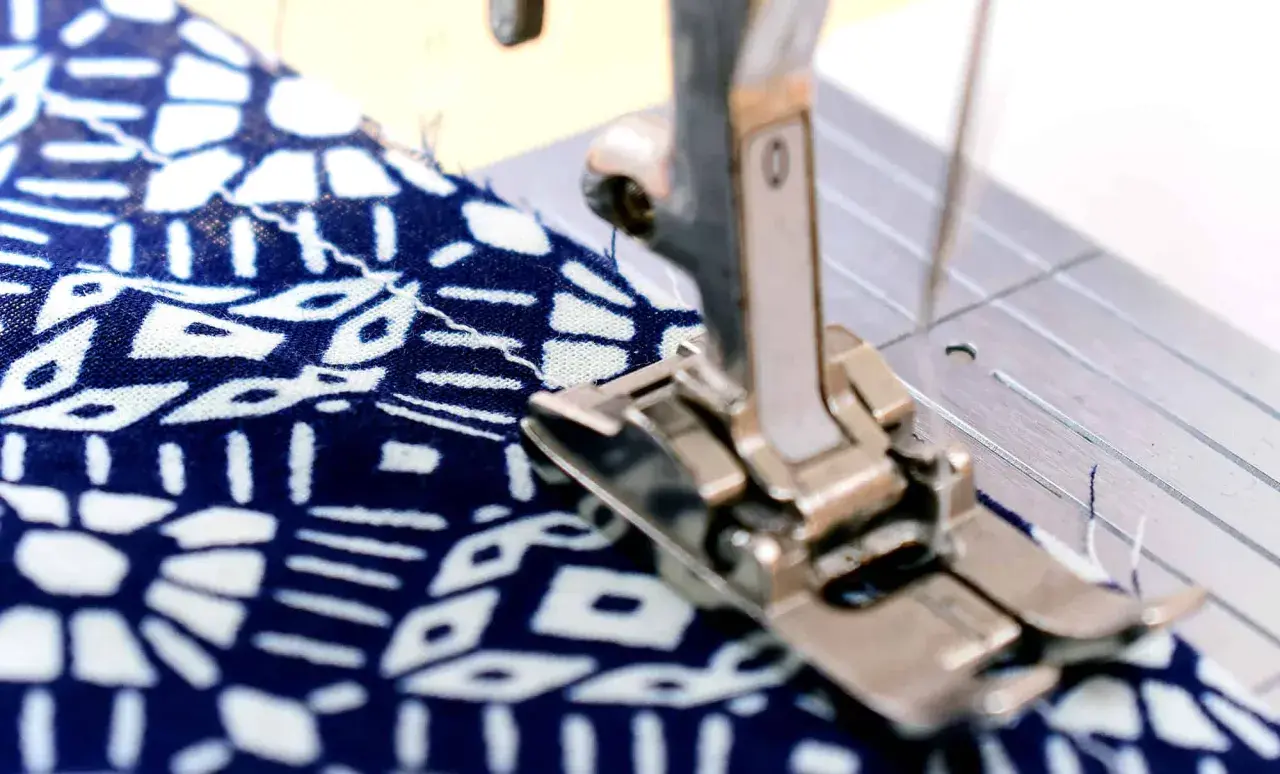 Sewing machine foot creating a narrow hem on a blue and white patterned fabric.
